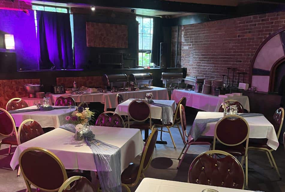 Large room set up for a group event with a catering station and tables with white tablecloths