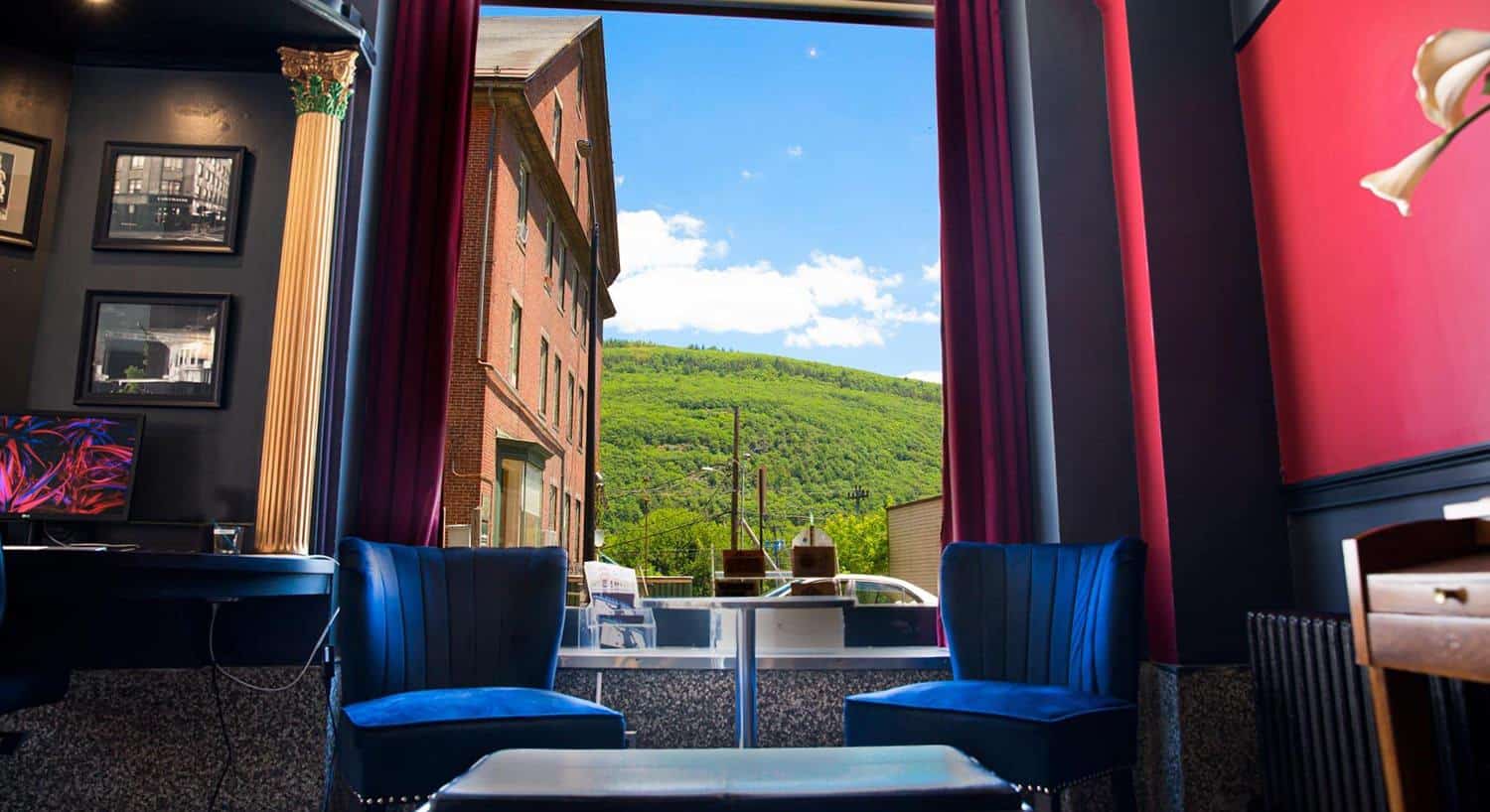 Sitting area with two blue velvet chairs and small table with large window with a view of a green tree covered mountain