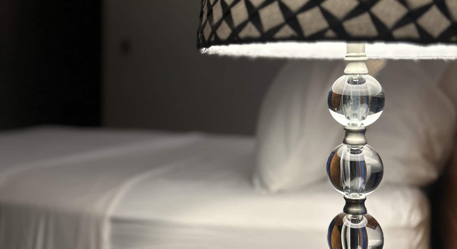 Close up view of glass beaded lamp and bed with white linens in the background