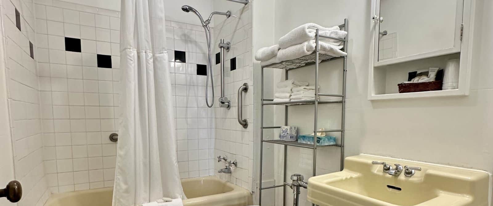 Bathroom with white walls, white with black accent tiled shower and tub combo, vanilla sink, and white cabinet with mirror