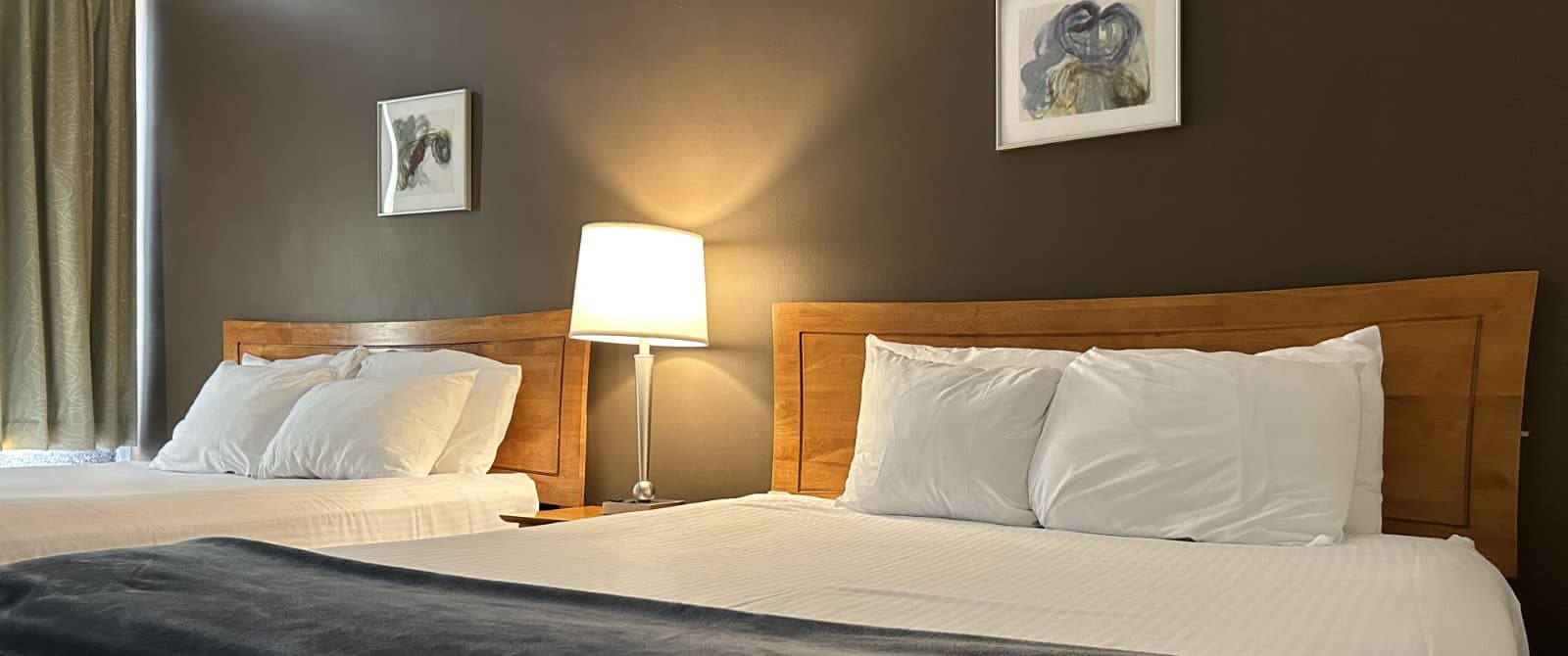 Bedroom with dark brown accent wall, two beds each with wooden headboard and white bedding, and nightstand with lamp