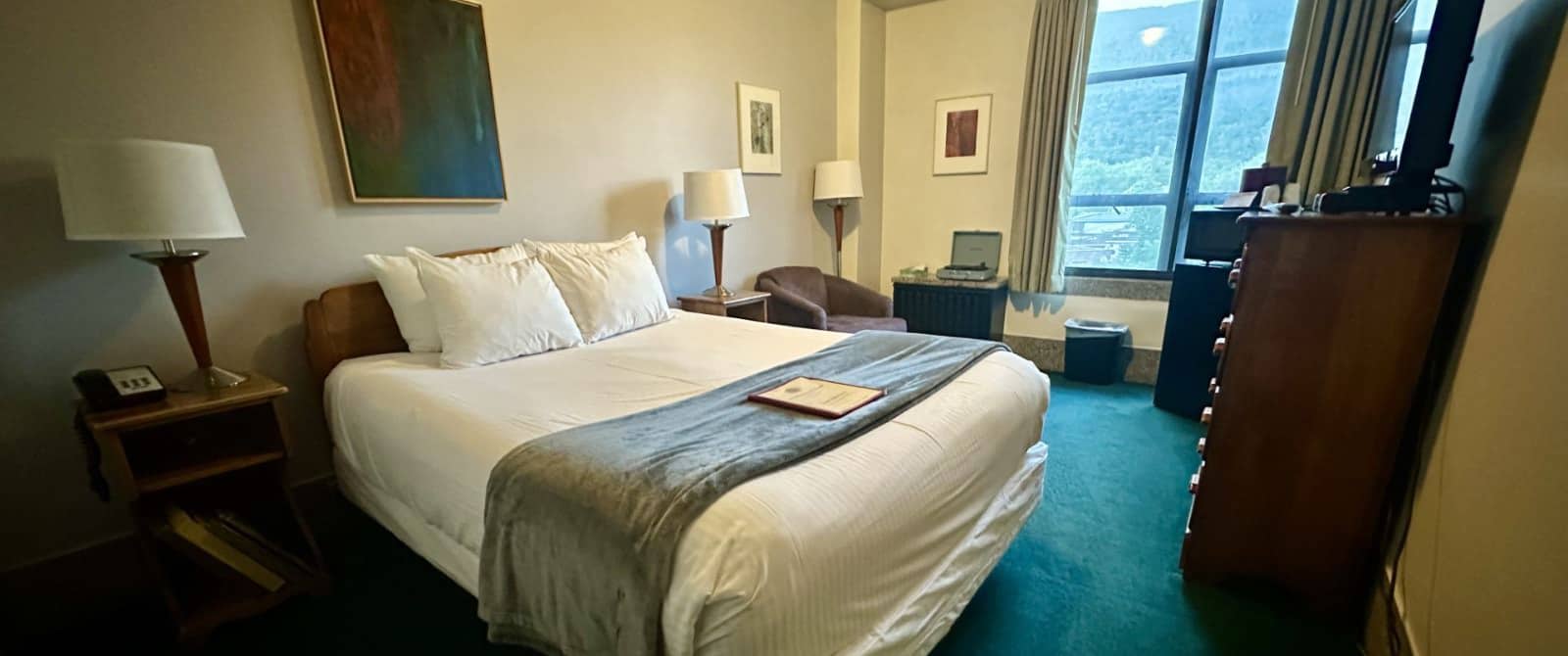 Bedroom with white walls, turquoise carpeting, wooden headboard, white bedding, and wooden nightstands with lamps