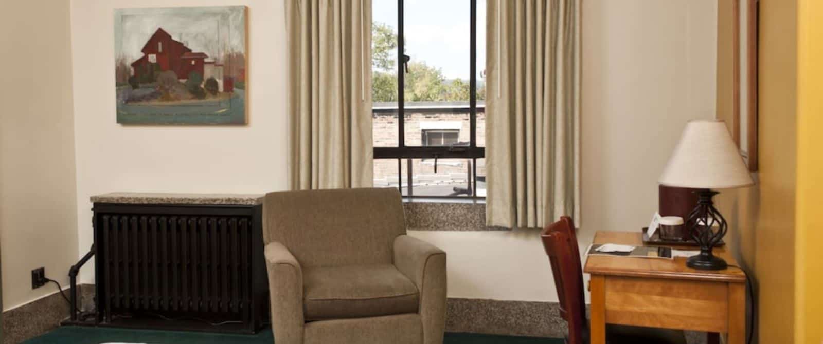 Bedroom with white and dark yellow walls, dark green carpeting, taupe upholstered armchair, and desk with chair