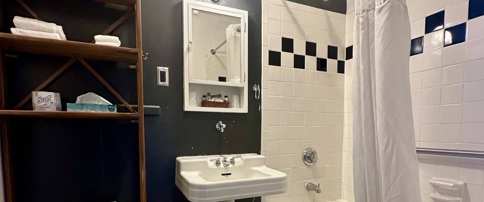 Bathroom with dark gray walls, white with black accent tiled shower and tub combo, white sink, and white cabinet with mirror