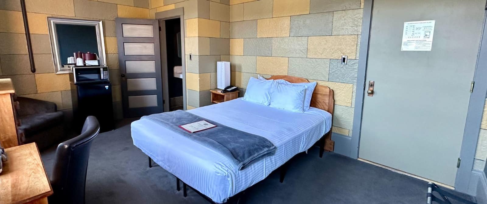 Bedroom with yellow and gray brick accent walls, wooden headboard, light blue bedding, microwave, and mini fridge