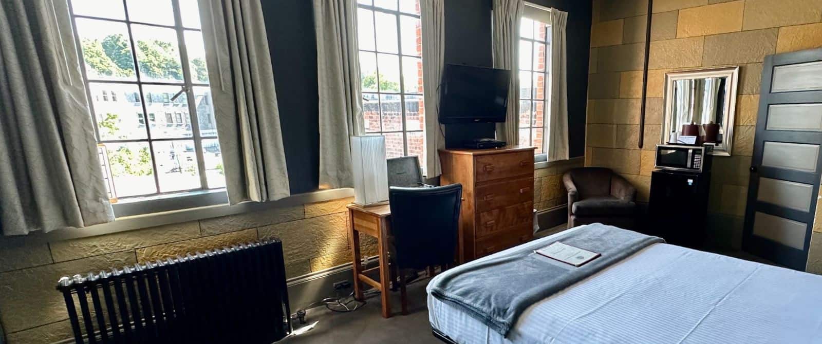 Bedroom with yellow and gray brick accent walls, wooden headboard, light blue bedding, microwave, mini fridge, wooden dresser, and desk with chair