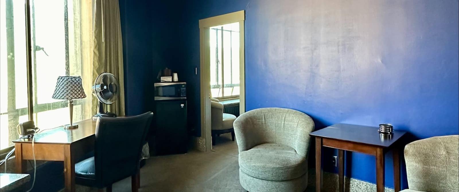 Bedroom with dark blue accent wall, light-colored carpeting, desk with chair, sitting area, mini fridge, and microwave