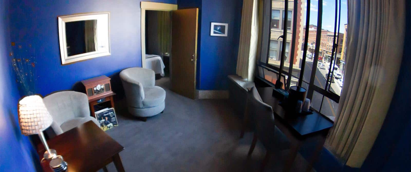 Adjoining room to bedroom with dark blue walls, light gray carpeting, sitting area, wooden table, and desk with chair