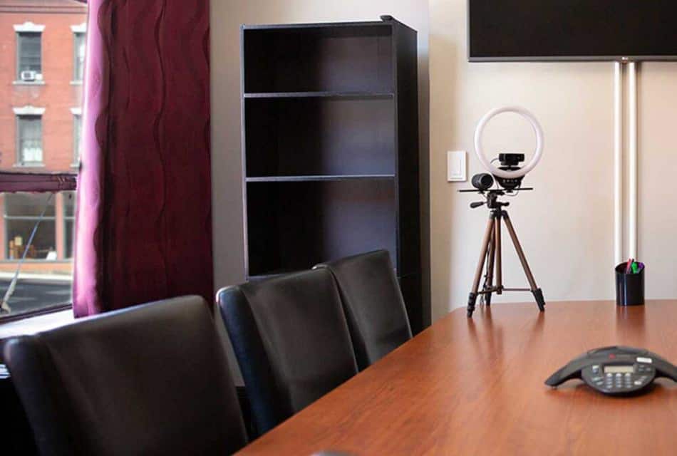 Conference room with white walls, burgundy curtains, black shelving unit, wooden table, black leather chairs, and conferencing equipment