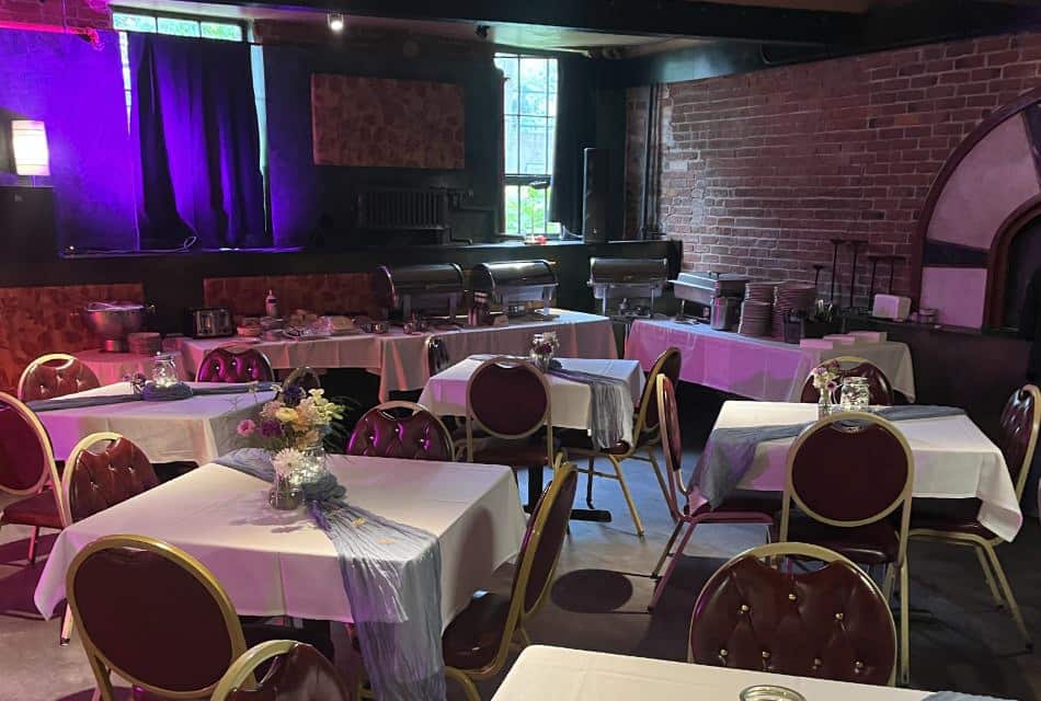 Large room set up for a group event with a catering station and tables with white tablecloths