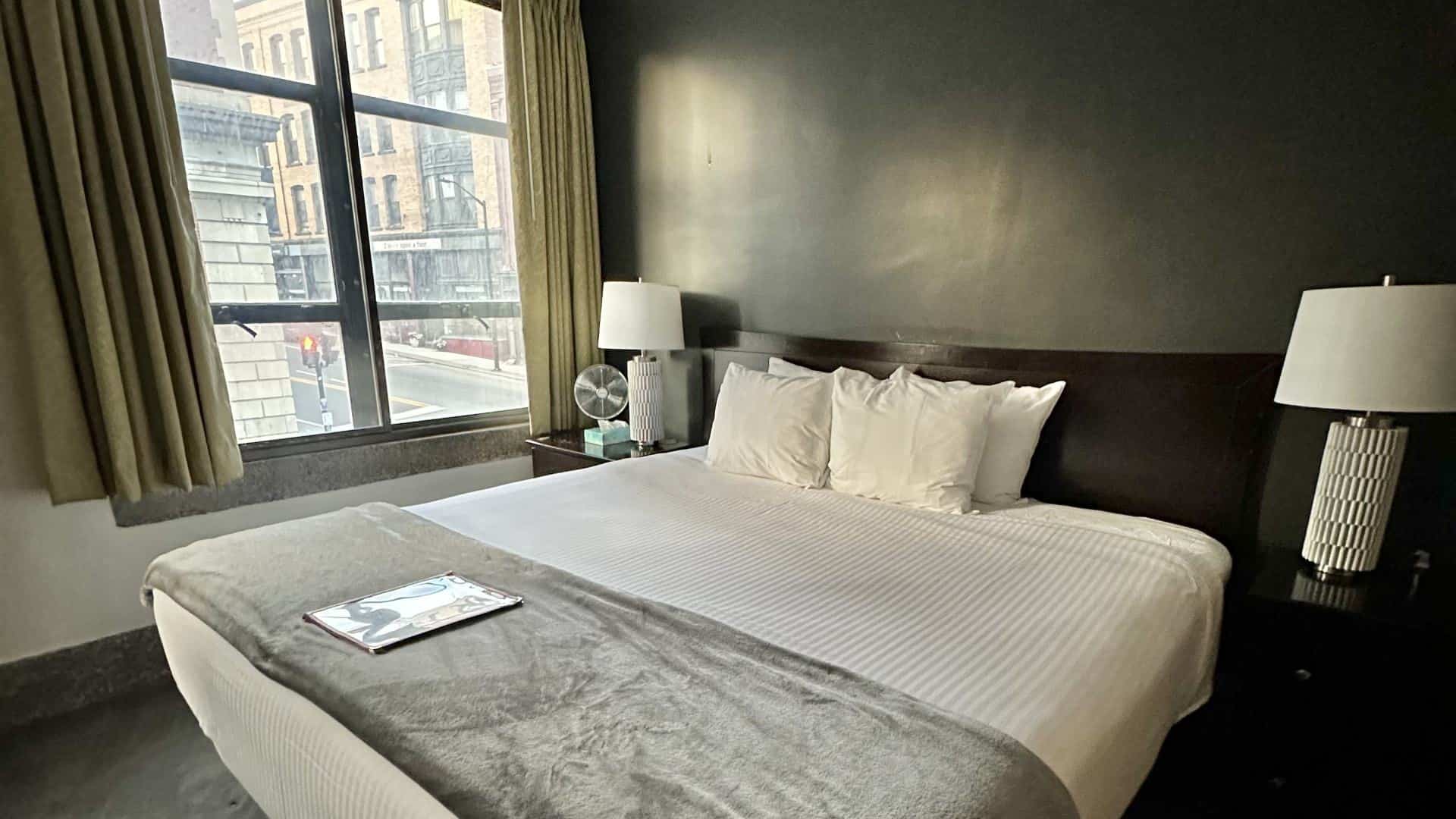 Bedroom with dark gray walls, dark wooden headboard, white bedding, and dark wooden nightstands with lamps