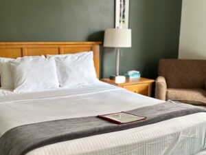 Bedroom with dark green walls, wooden headboard, white bedding, and wooden nightstand with lamp