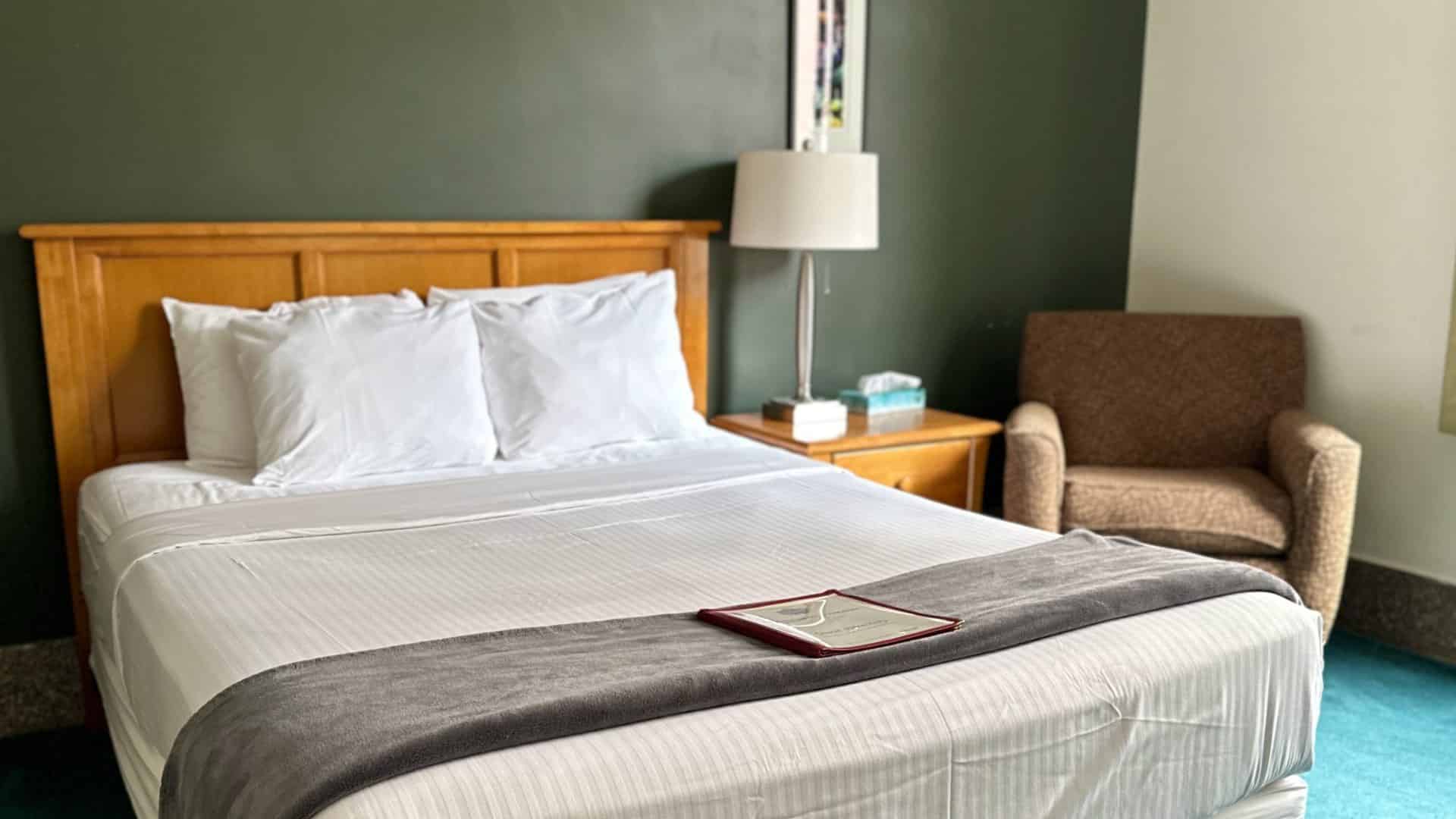 Bedroom with dark green walls, wooden headboard, white bedding, and wooden nightstand with lamp