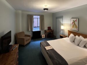 Bedroom with light gray walls, emerald carpeting, wooden headboard, white bedding, and desk with chair