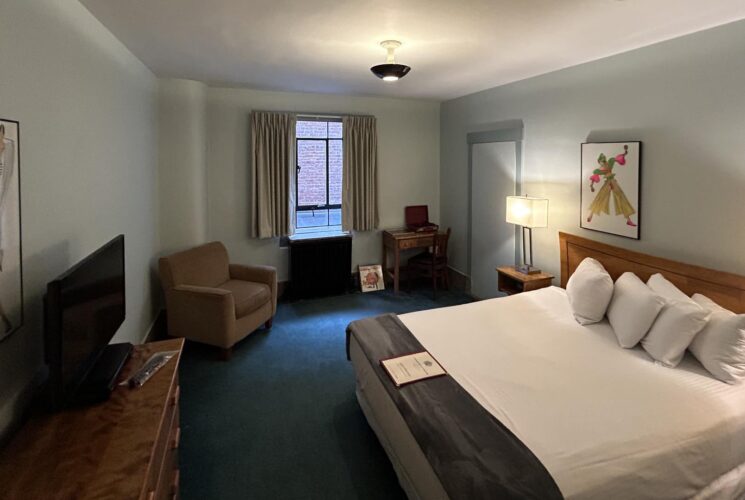 Bedroom with light gray walls, emerald carpeting, wooden headboard, white bedding, and desk with chair