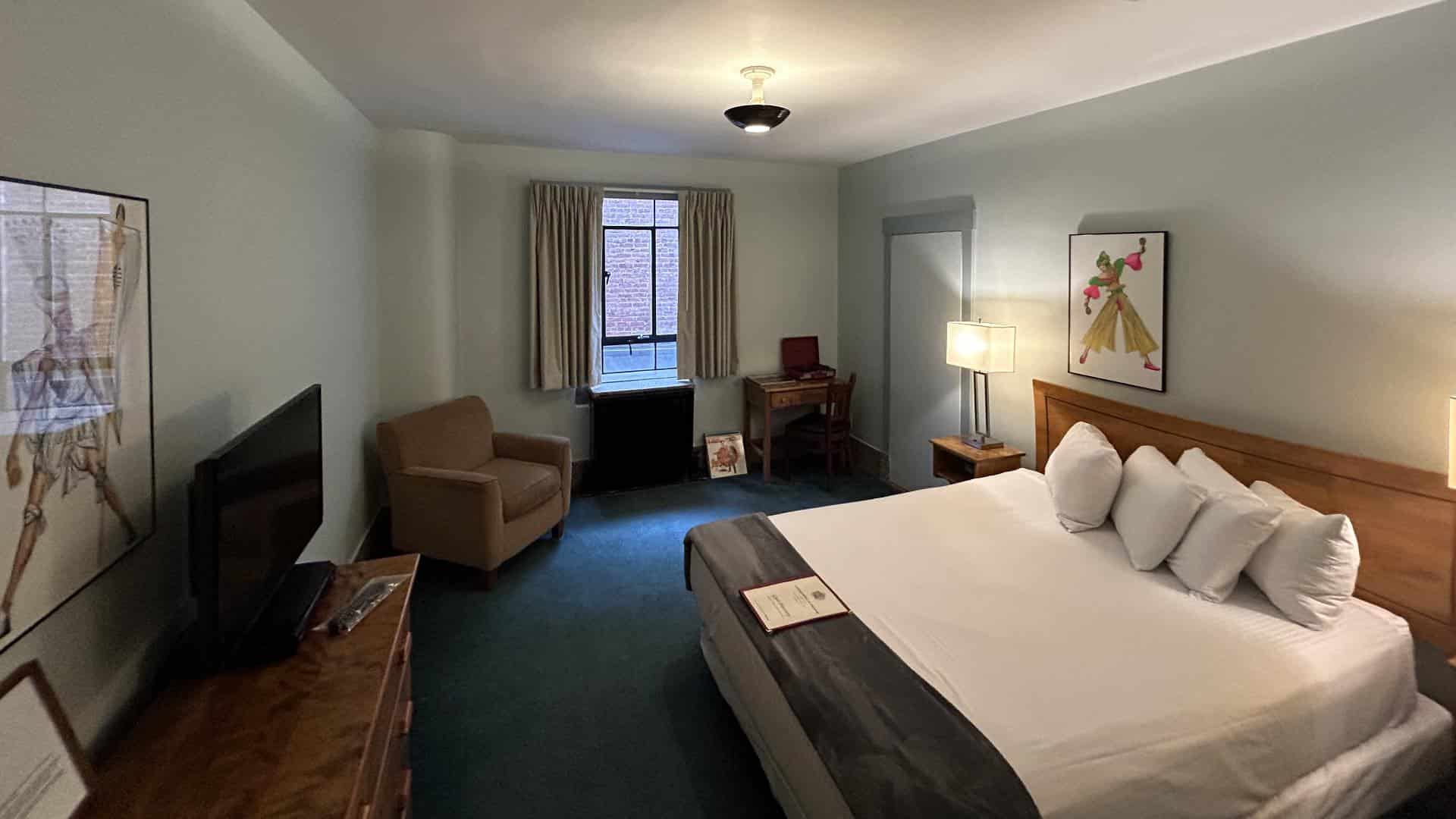 Bedroom with light gray walls, emerald carpeting, wooden headboard, white bedding, and desk with chair