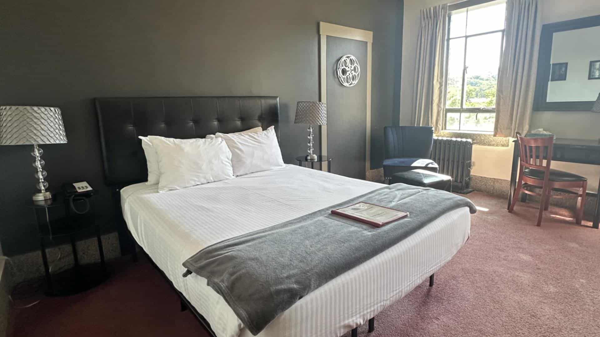 Bedroom with dark gray walls, black leather headboard, white bedding, and black wooden nightstands with lamps