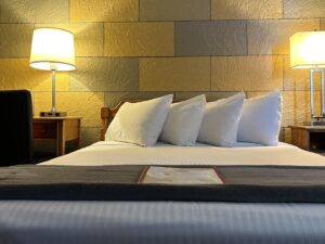 Bedroom with yellow and gray brick accent wall, wooden headboard, white bedding, and wooden nightstands with lamps