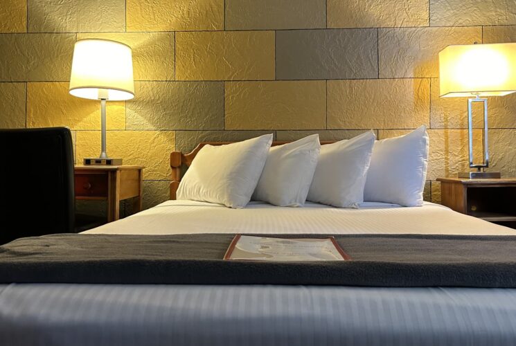 Bedroom with yellow and gray brick accent wall, wooden headboard, white bedding, and wooden nightstands with lamps