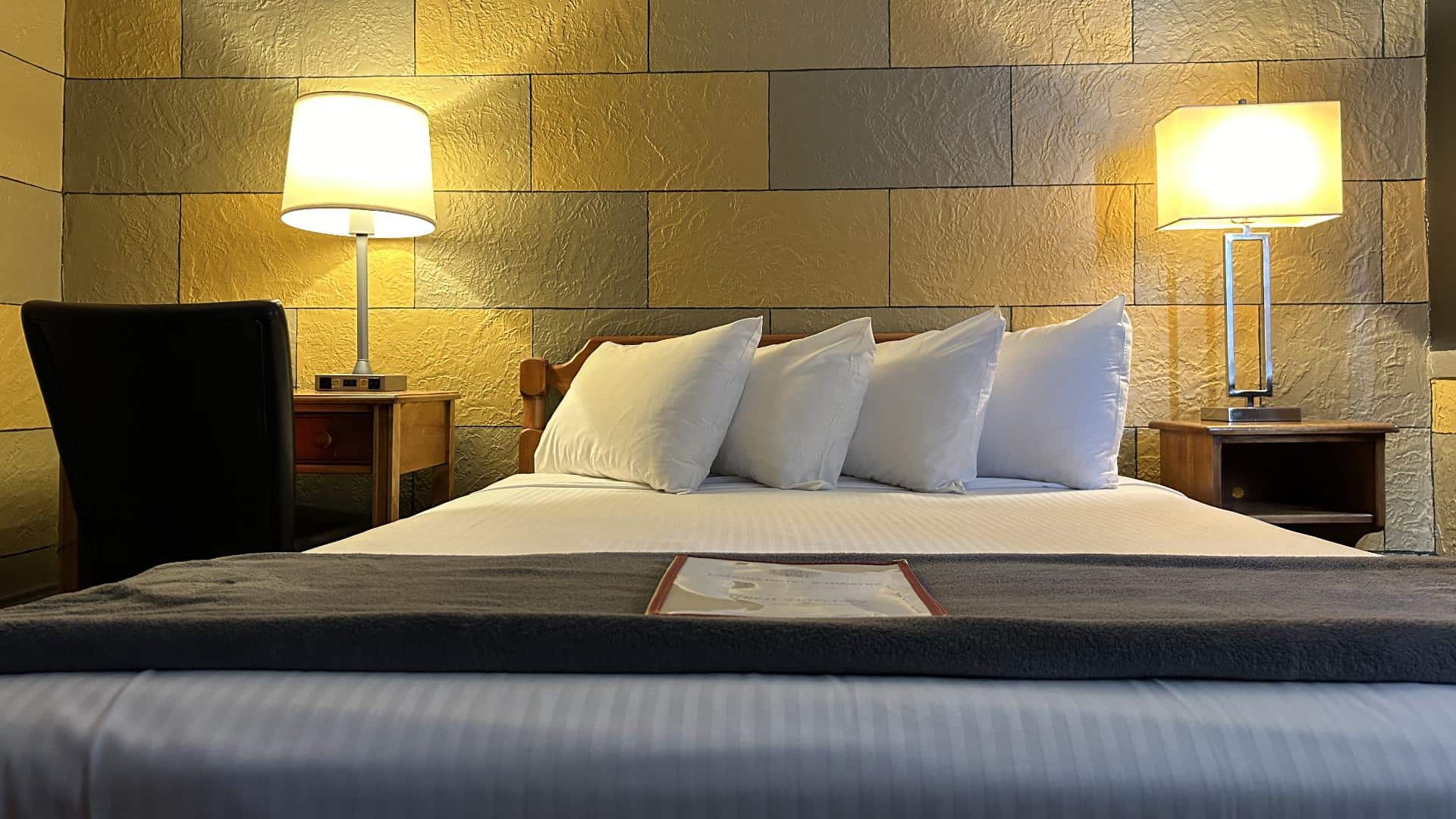 Bedroom with yellow and gray brick accent wall, wooden headboard, white bedding, and wooden nightstands with lamps