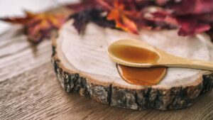 maple syrup on spoon and piece of wood, leaves in backdrop.