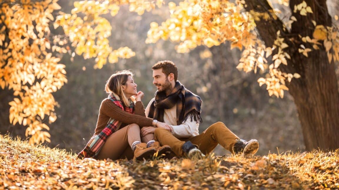 a couple sitting on a hill in a park during fall