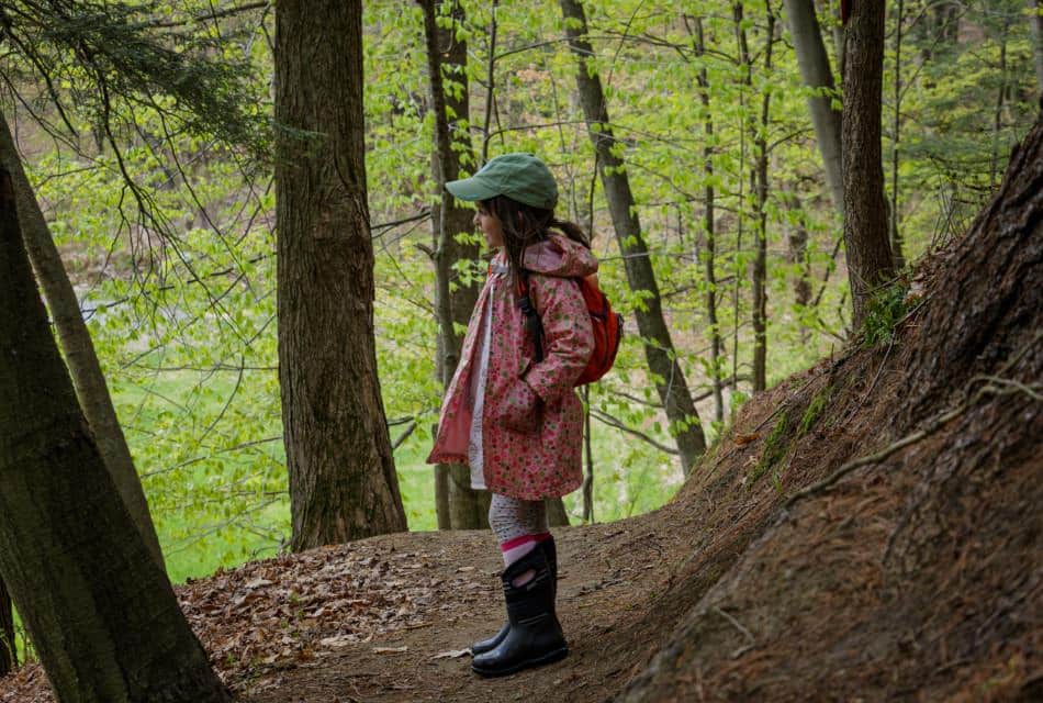 Young child dressed in hiking gear standing on trail in mountains